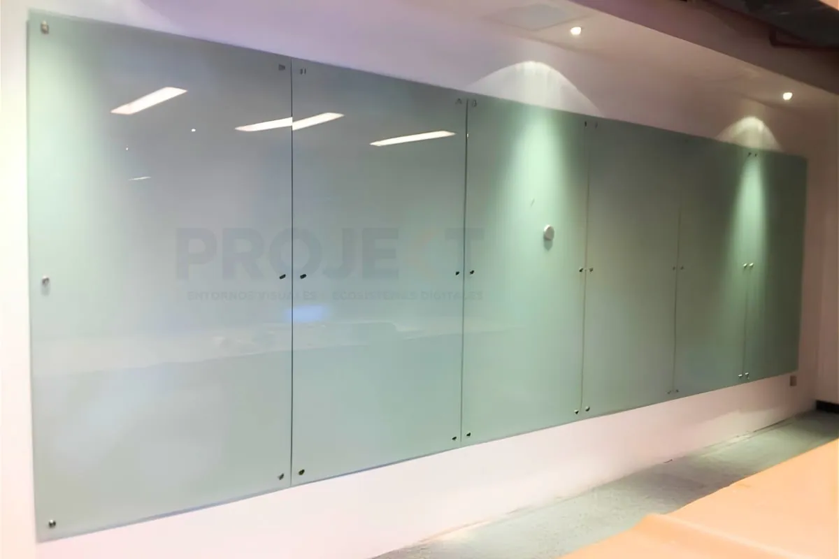 Pizarra de cristal con logo corporativo y repisa de acero instalada en un muro blanco